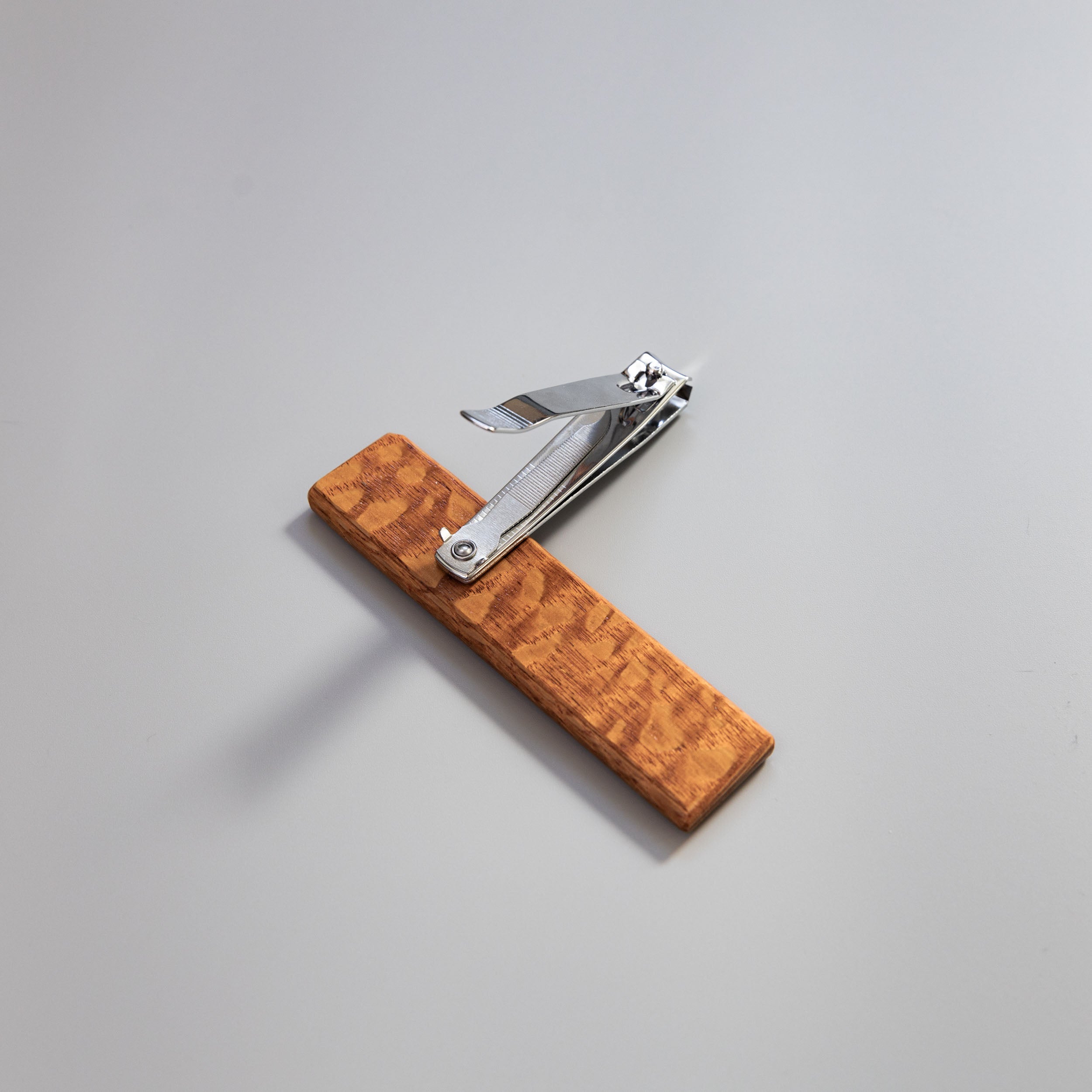 Charleston Nail Clipper Company’s showcasing their stainless steel nail trimmer’s 360-degree pivot on a wooden base for precision & control.  Leopard wood clippers on a grey background.