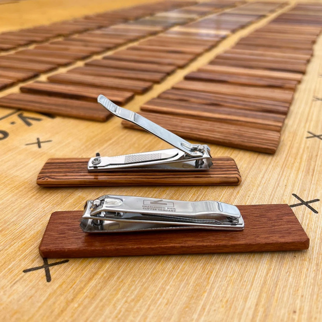 Hand-crafted nail clippers with dark wooden bases laying side by side with an array of exotic local woods used for the curation & design of the nail trimmers. 