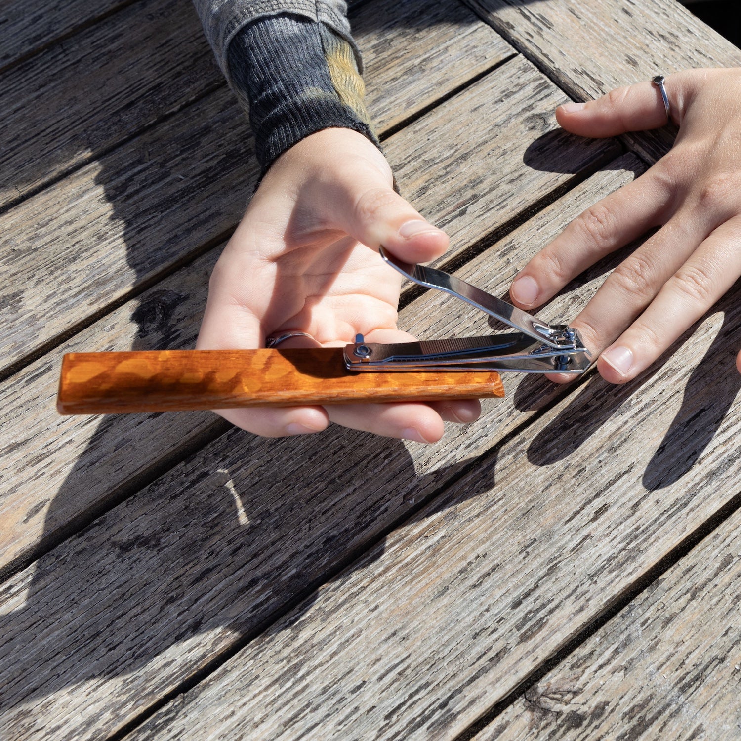 Nail trimmers extended 90 degrees to showcase the pivot design while a hand is holding the ergonomic wooden base about to trim nails. 